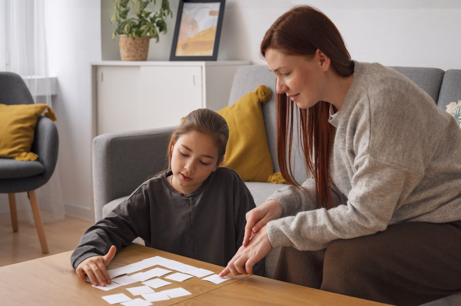 A mother-figure and a young girl playing a card matching game at a coffee table at home