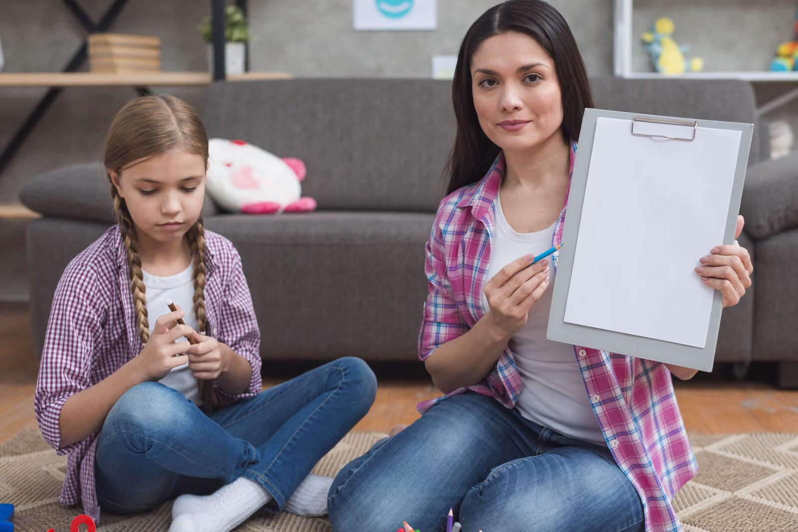 A practitioner sitting on the floor with a young girl, showing a clipboard during a support session